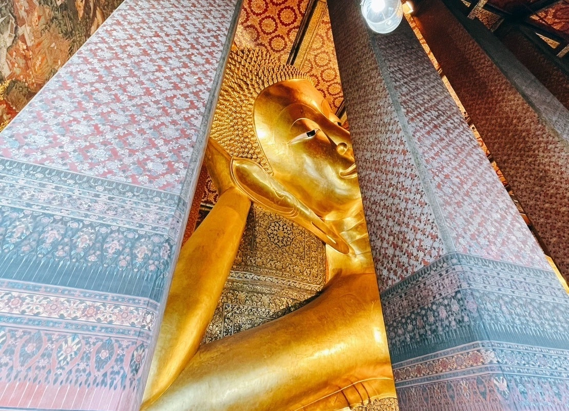 Colossal Reclining Buddha at Wat Pho in the beautiful hall decorated by pillars with Thai art pattern and mural at ceiling